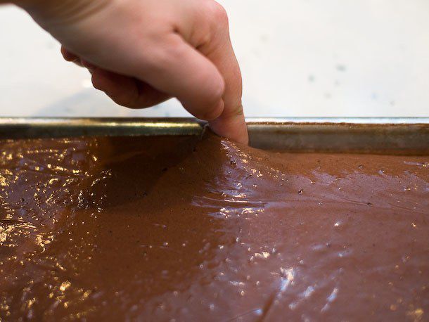 A finger is dragged around the periphery of the jelly roll pan full of cake batter.