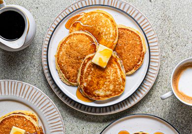 Plate of extra light and fluffy buttermilk pancakes topped with pat of butter and drizzled with maple syrup displayed against a grey speckled background