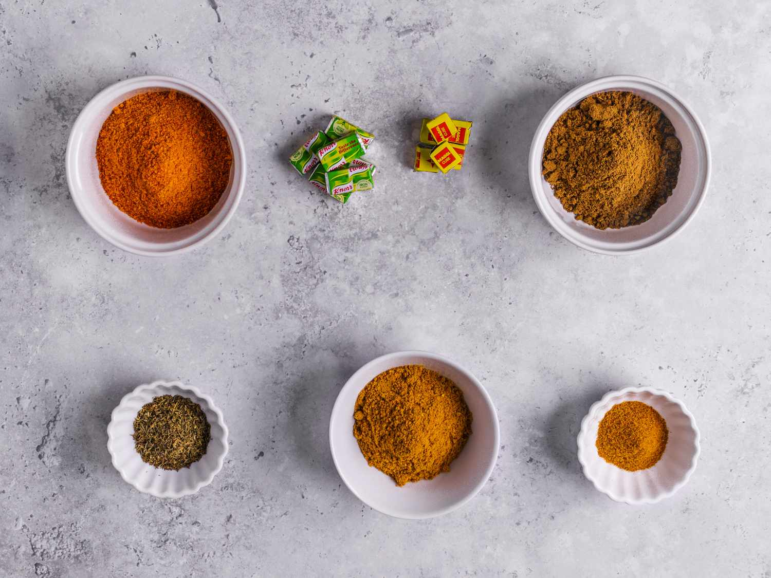 Spices nicely arranged in white bowls on a marbled grey backdrop