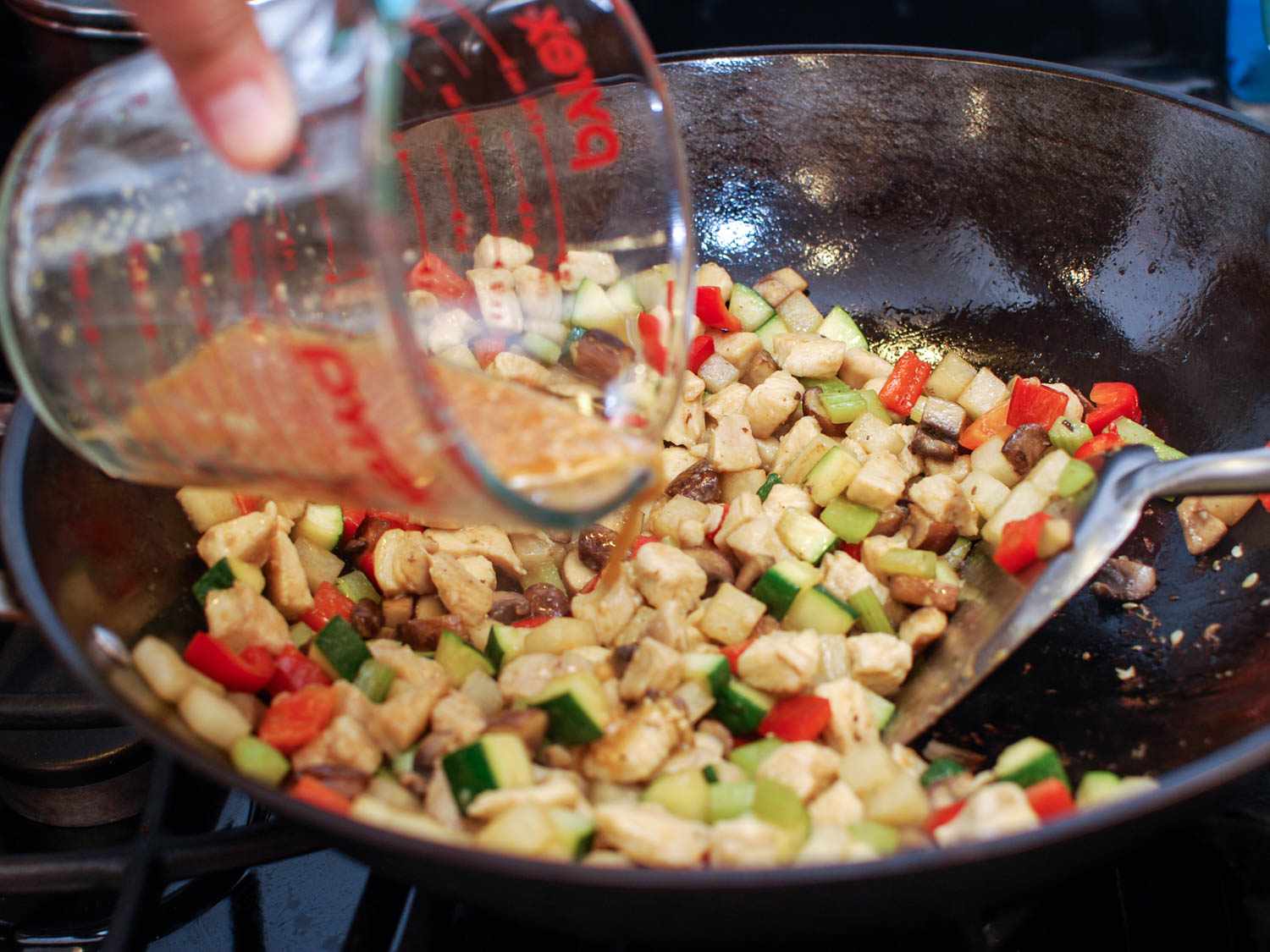 Adding the sauce into the wok with chicken and vegetables for cashew chicken ding.