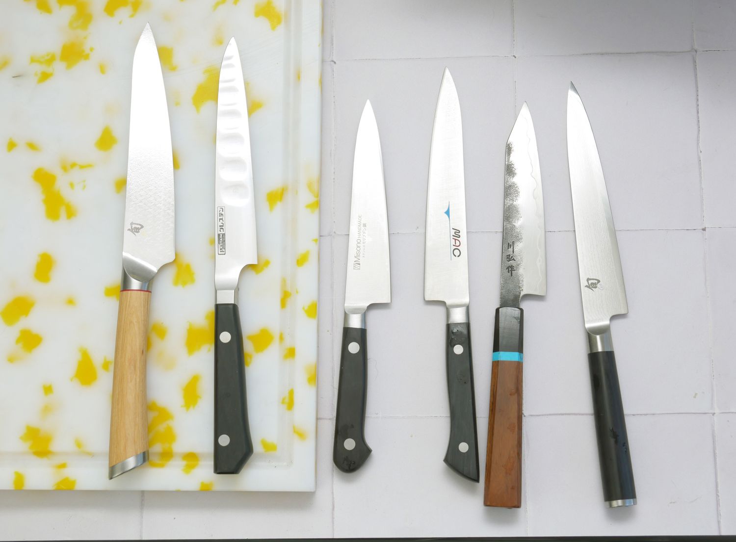 A set of six kitchen knives with different handles and blade shapes arranged on a white surface