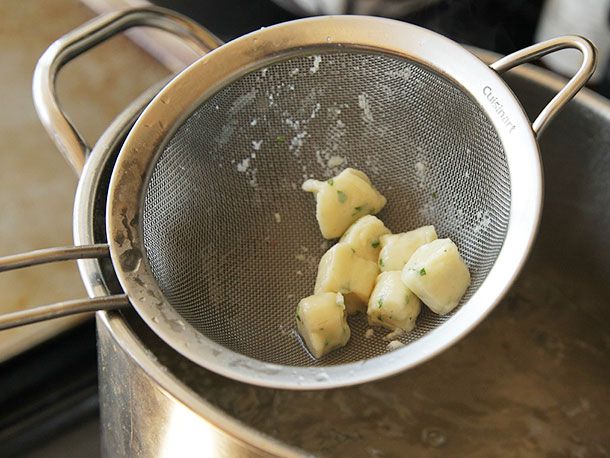 7 Parisian gnocchi are held up to the camera in a fine-mesh strainer.