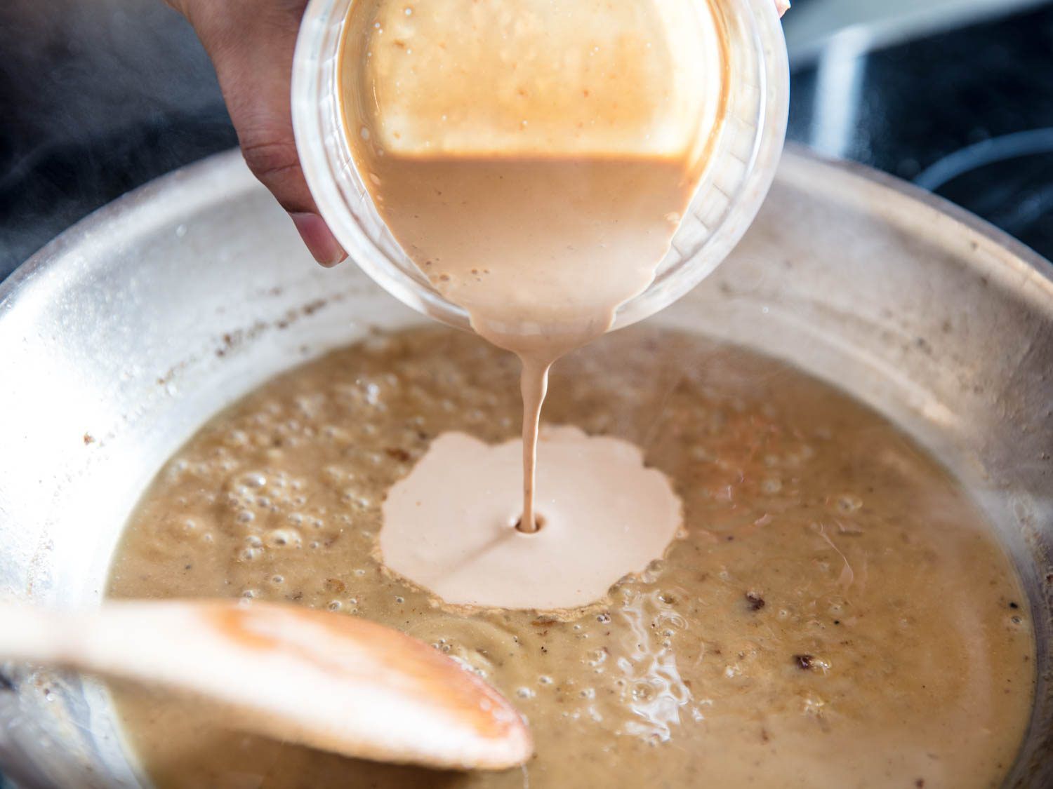 Toasted cream being poured into a stainless steel skillet where a pan sauce for meat is being made.
