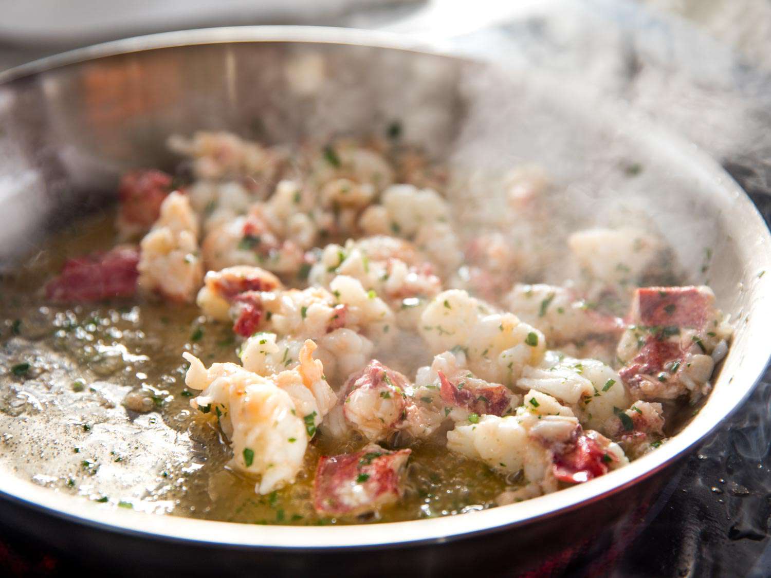 Cooked lobster meat being sautéed in butter, getting showered with minced fresh herbs.