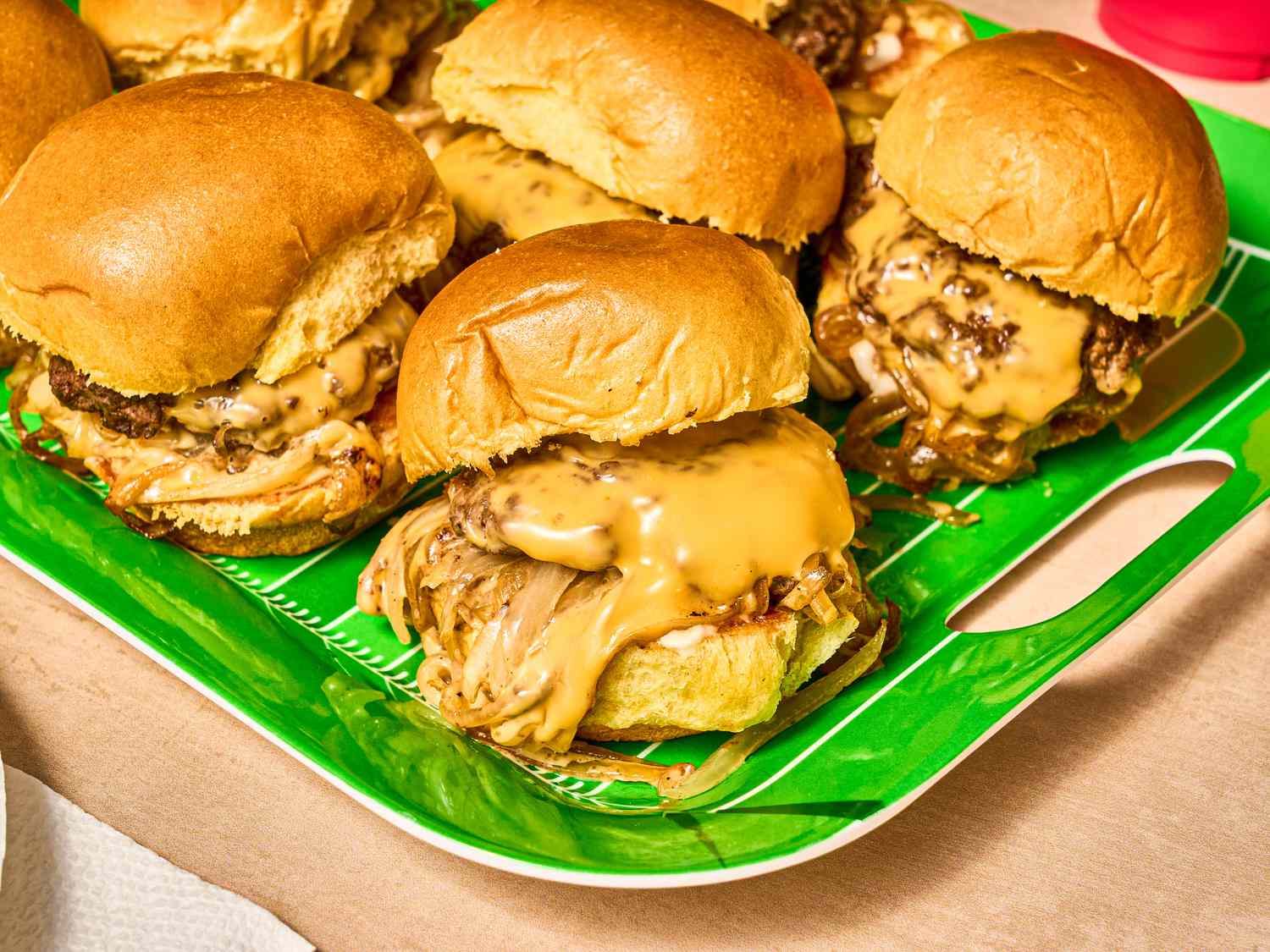 Bright green platter of sliders with overflowing cheese and onions 