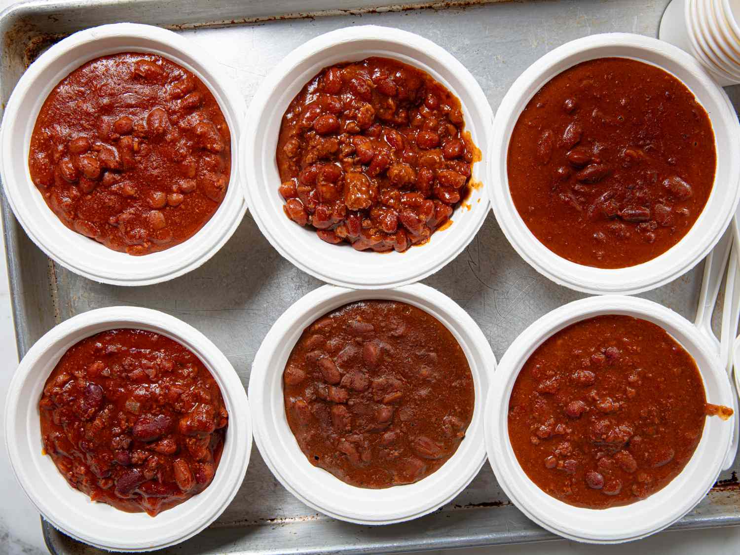 Six bowls of chili arranged on a tray each displaying a different type of canned chili for taste testing