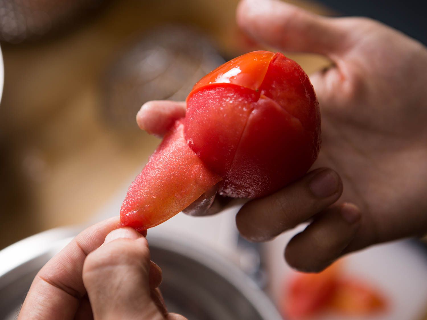Skin is pulled from a blanched plum tomato.