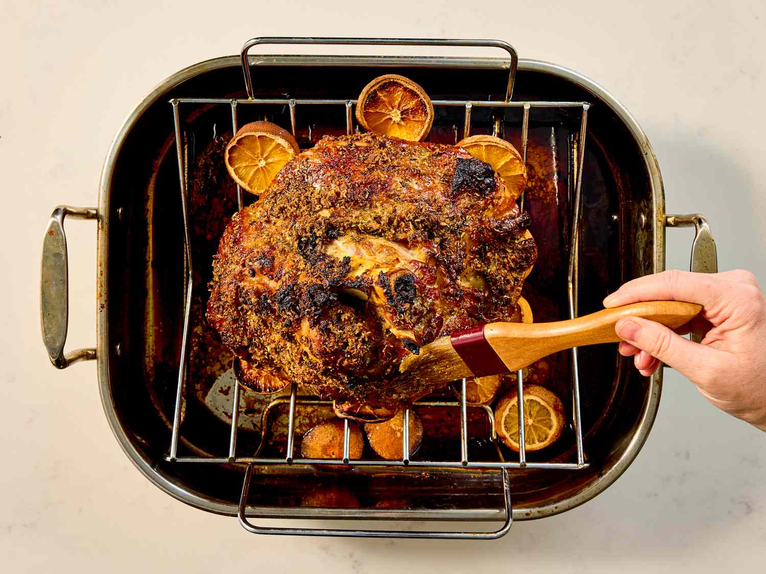 A slowroasted ham with a hand basting it in a roasting pan accompanied by sliced oranges