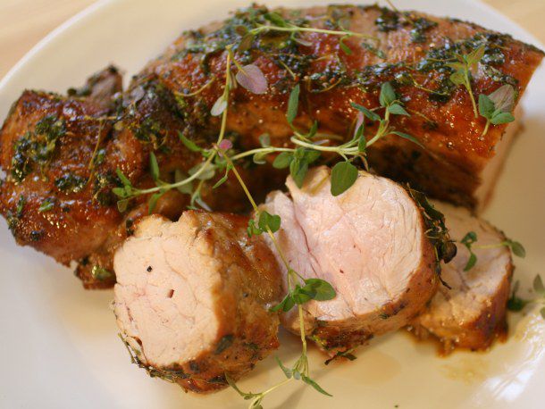 Closeup of honey-thyme roasted pork loin, served on a plate with a garnish of thyme sprigs.