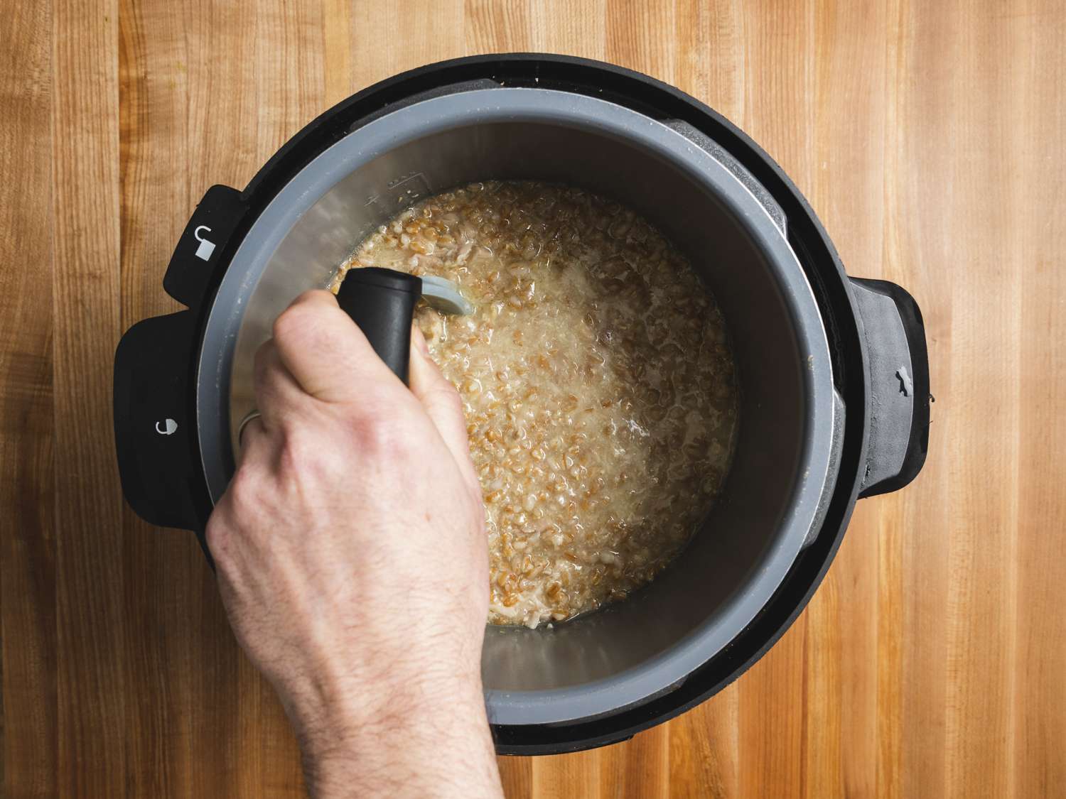 Overhead view of a hand mashing farro and chicken in pressure cooker. 