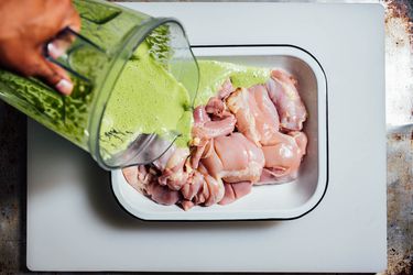 Mint-yogurt marinade being poured over boneless skinless chicken thighs