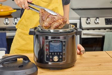 A person removes cooked meat from the Instant Pot Pro 10-in-1 6-Quart Pressure Cooker