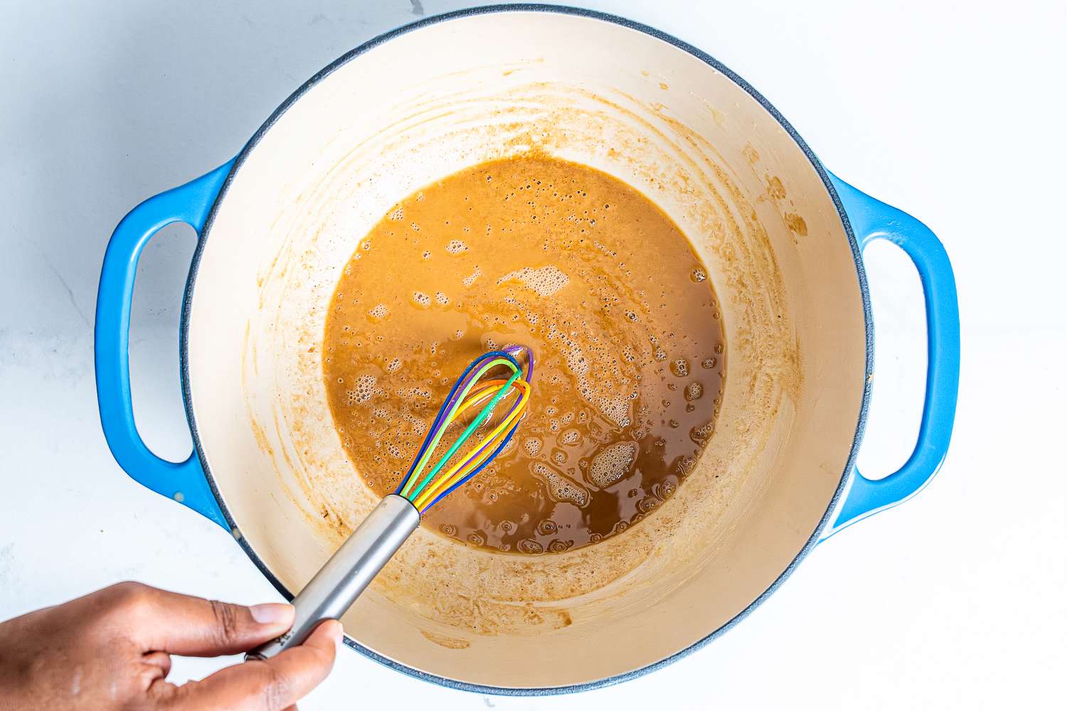 A hand using the Kuhn Rikon Silicone Rainbow Whisk to whisk a sauce in a pot