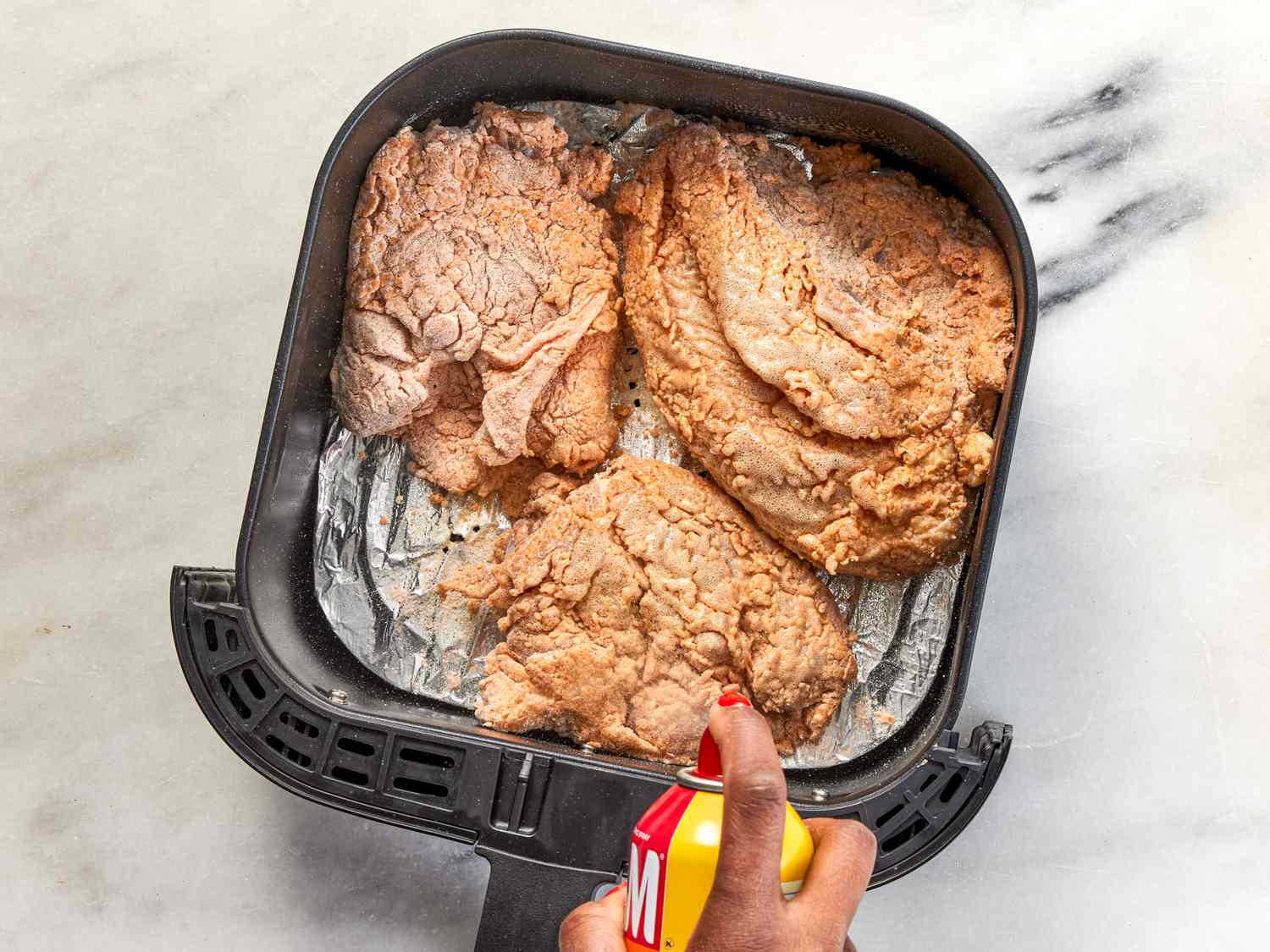 Spraying chicken with cooking spray in air fryer
