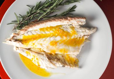 An overhead view of a piece of branzino drizzled with citrus vinaigrette on a while plate next to sprigs of fresh rosemary.