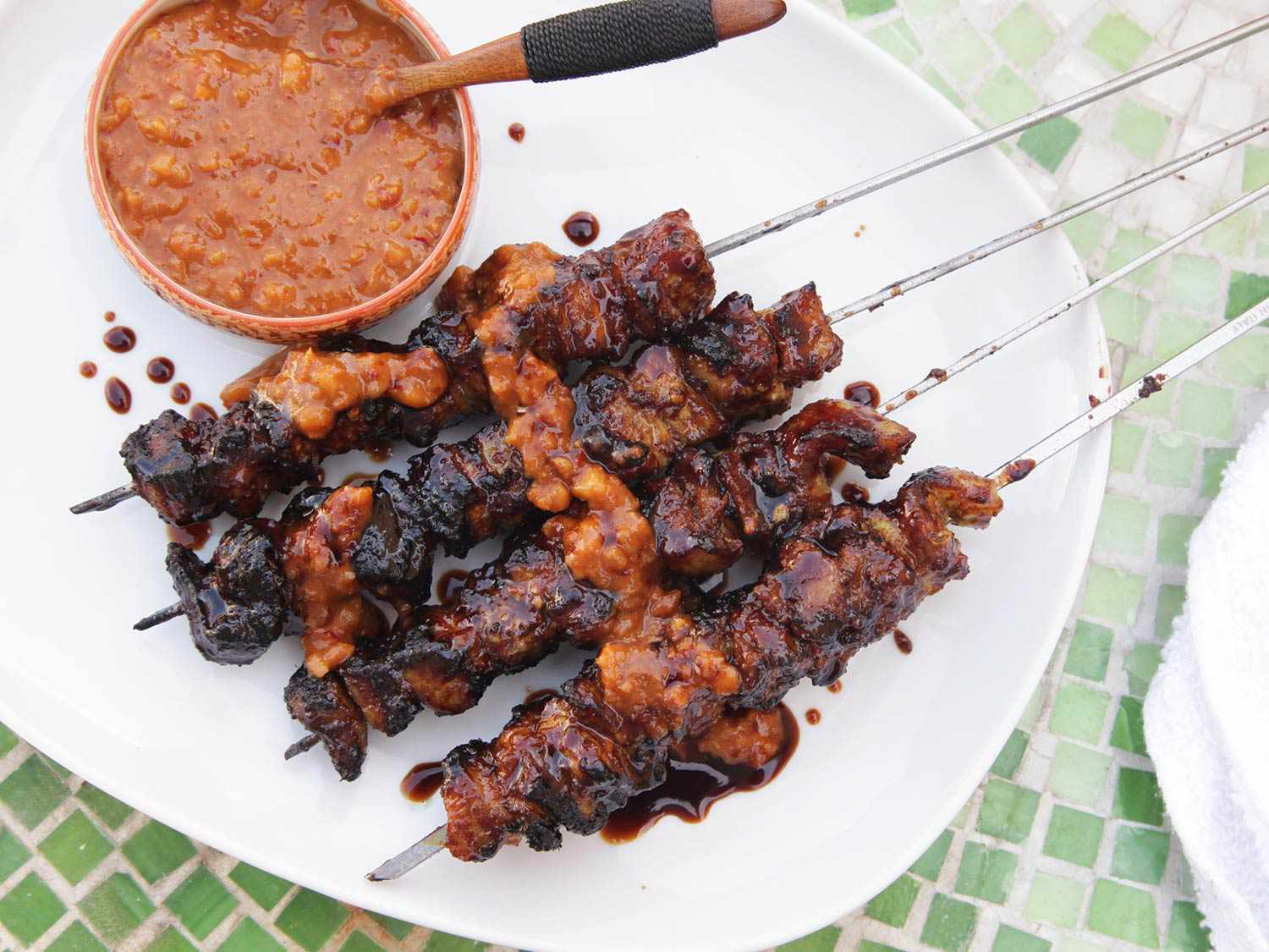 Chargrilled Balinese pork satays on a plate with peanut sauce.