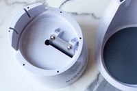 Interior view of a plastic container with a metal attachment of Hawaiian Shaved Ice HomePro Shave Ice and Snow Cone Machine (S777) piece, alongside its lid resting on a marble surface