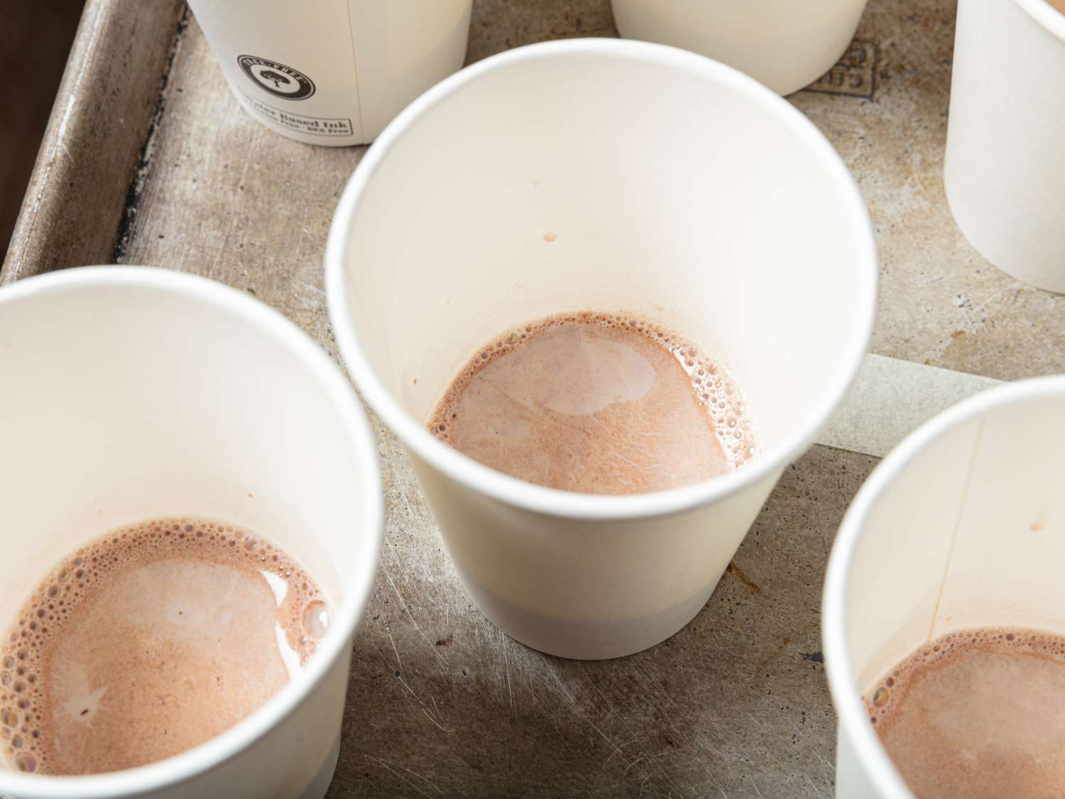 Several small white cups with hot chocolate in them on sheet pan
