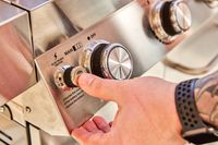 Hand pressing a button on the Monument Grills Stainless 4-Burner Propane Gas Grill