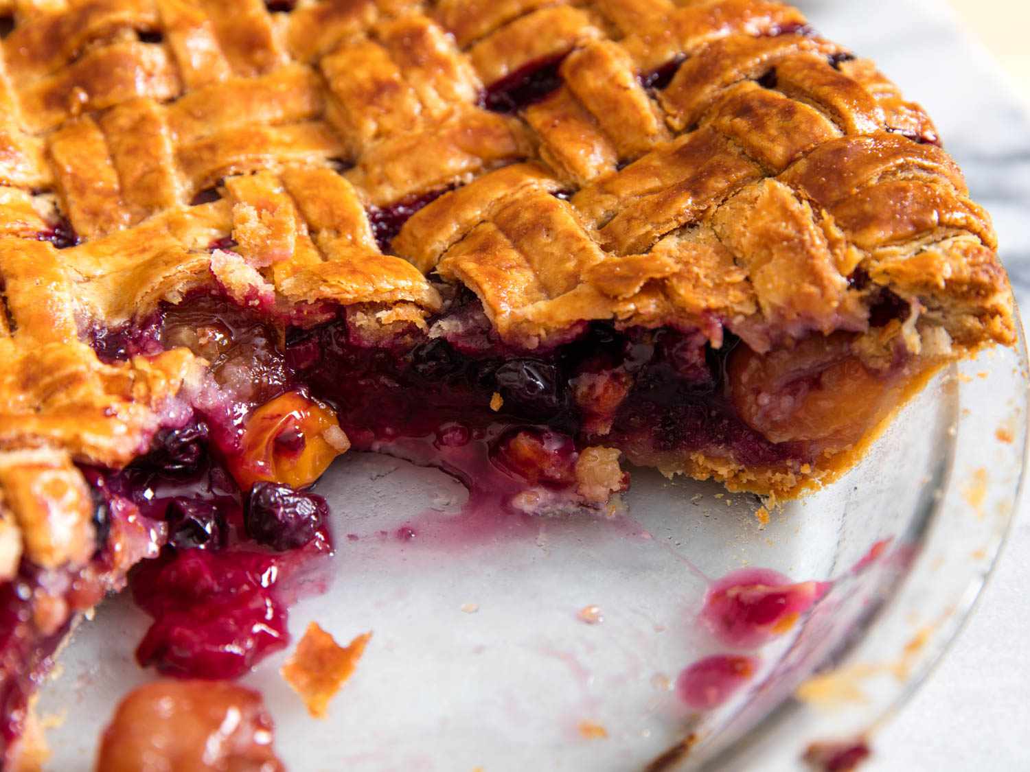 A mixed-fruit pie with a lattice top in a Pyrex dish, with some of the pie missing