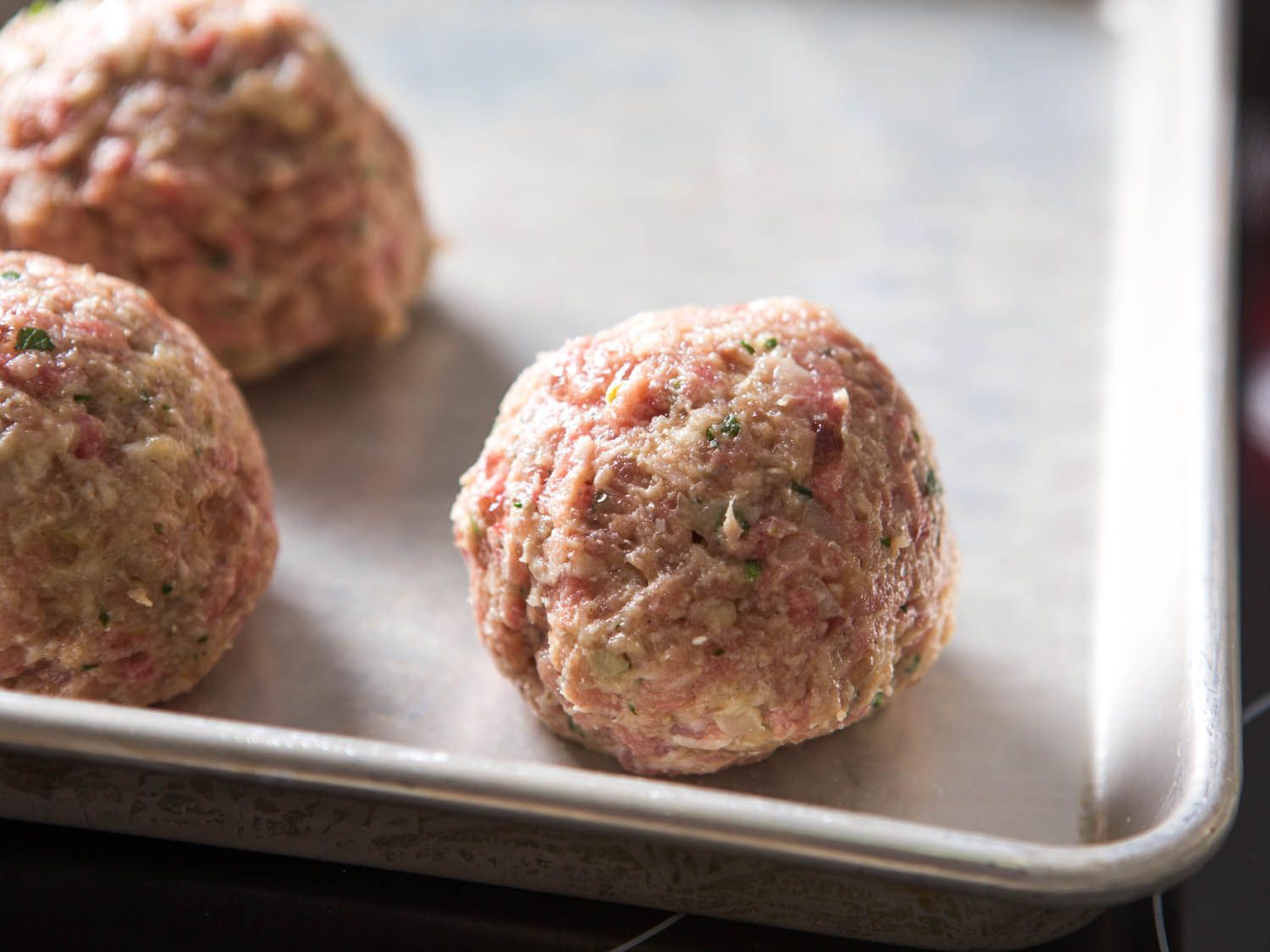 Rolled meatballs on a rimmed sheet pan before broiling.