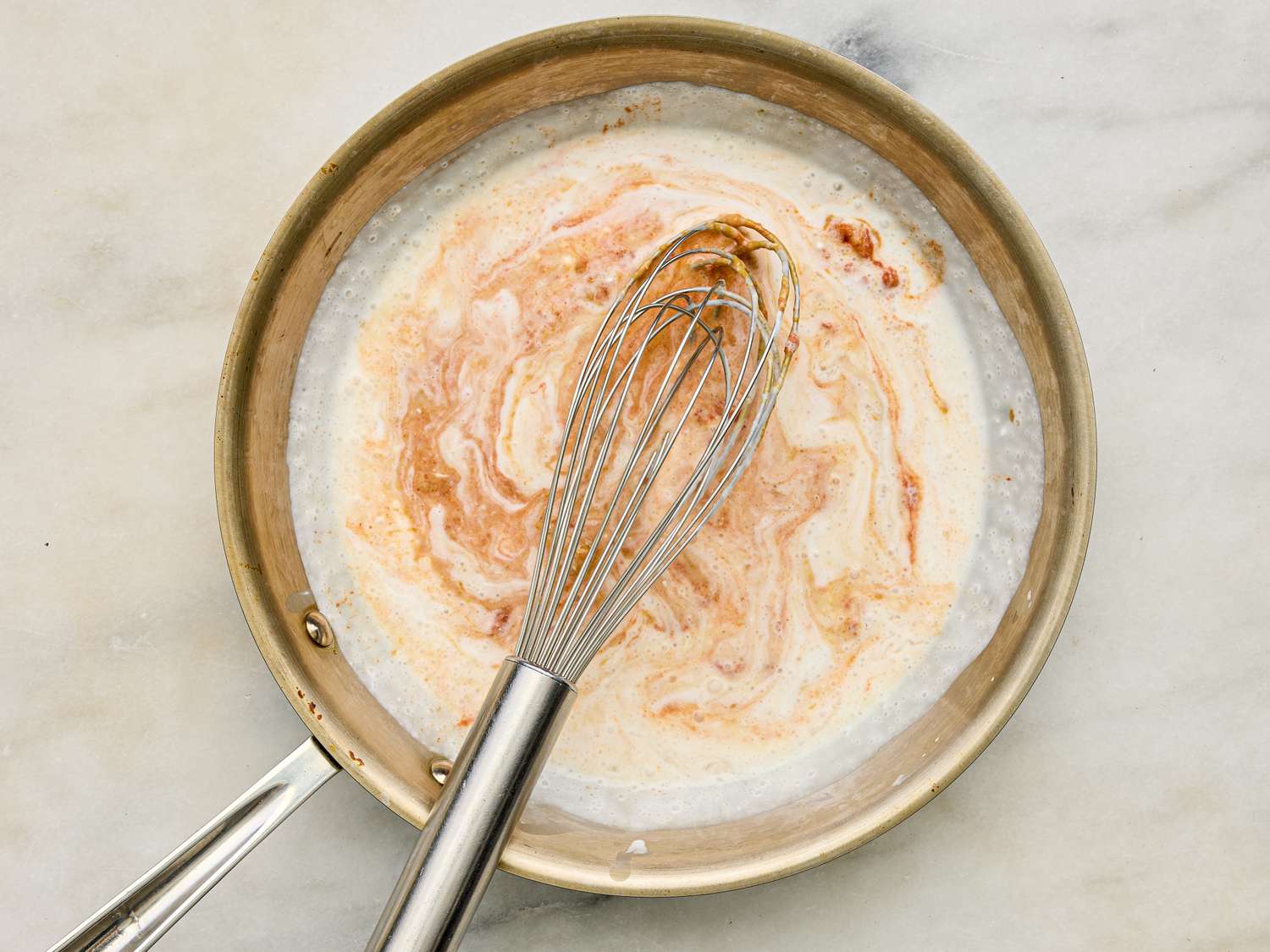 A whisk in a pan with cream being stirred into a sauce