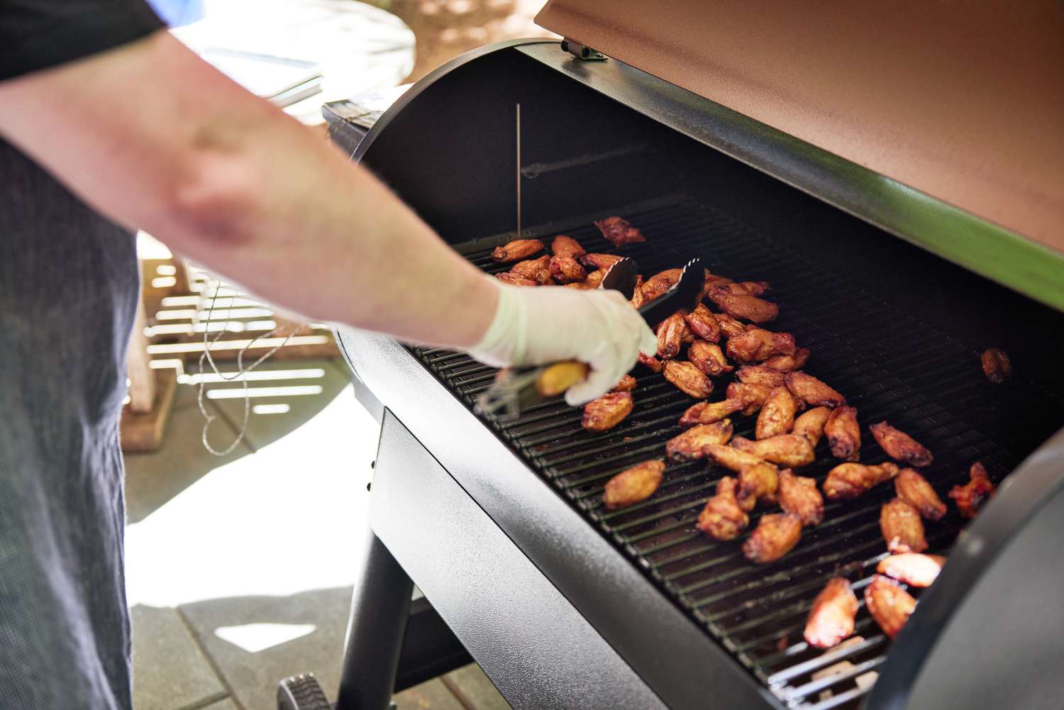 A person using tongs to flip chicken wings on a pellet grill