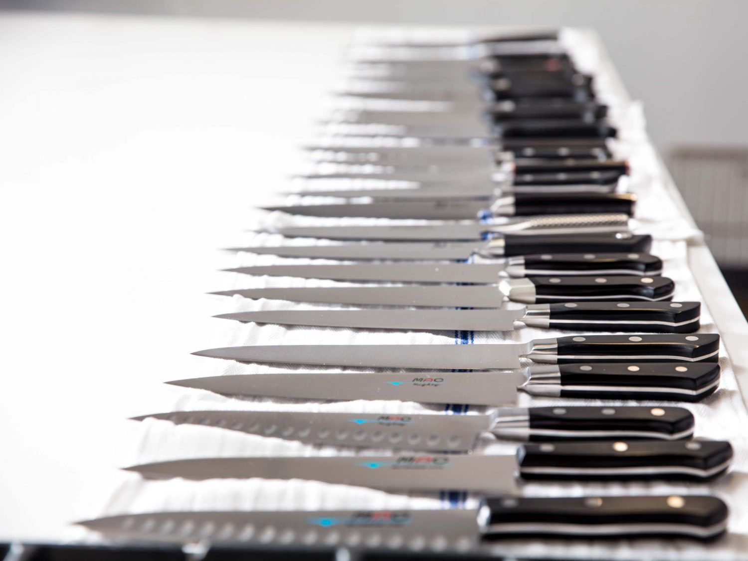 Many chef's knives lined up on kitchen towels