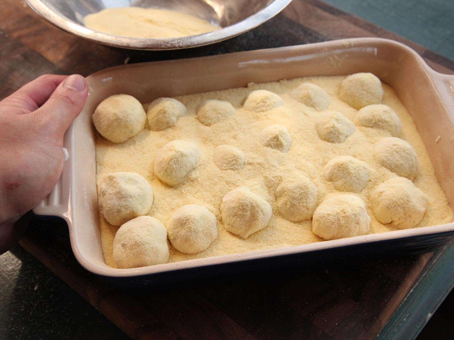 Gnudi resting in a baking dish filled with semolina.
