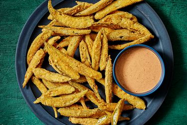 Dark blue plate with fried okra and a bowl of comeback sauce, on a deep green surface