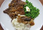 Pot roast on a white plate with buttered peas, mashed potatoes and gravy. 