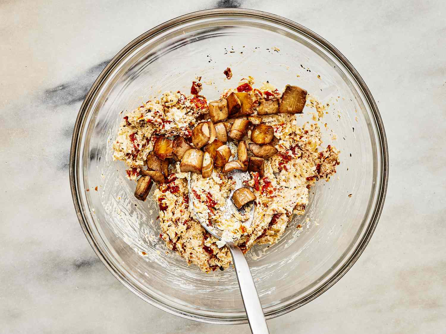 Mushroom stems, cream cheese, Parmigiano-Reggiano, panko, sun dried tomatoes and seasonings mixed in a glass bowl with spoon
