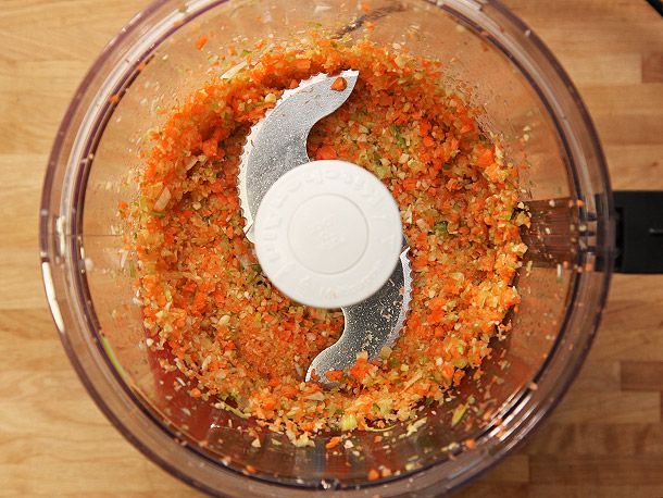 Overhead view of finely chopped aromatics in the bowl of a food processor, ready for sweating.