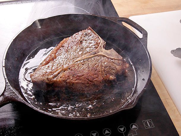 A Porterhouse steak searing in smoking oil in a cast iron skillet.