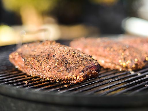 Duck breasts coated in a crust of spices on the grill of a barbecue 