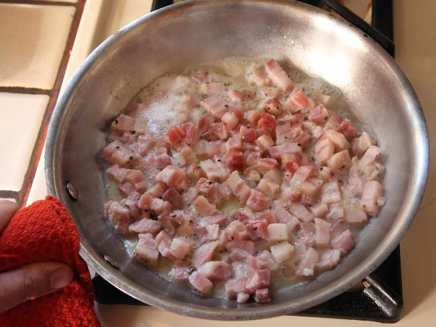 Overhead of diced pancetta being cooked in a skillet.
