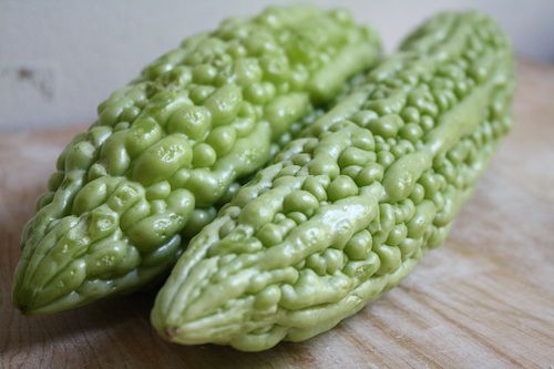 Closeup of two bitter melons placed on a wooden work surface.