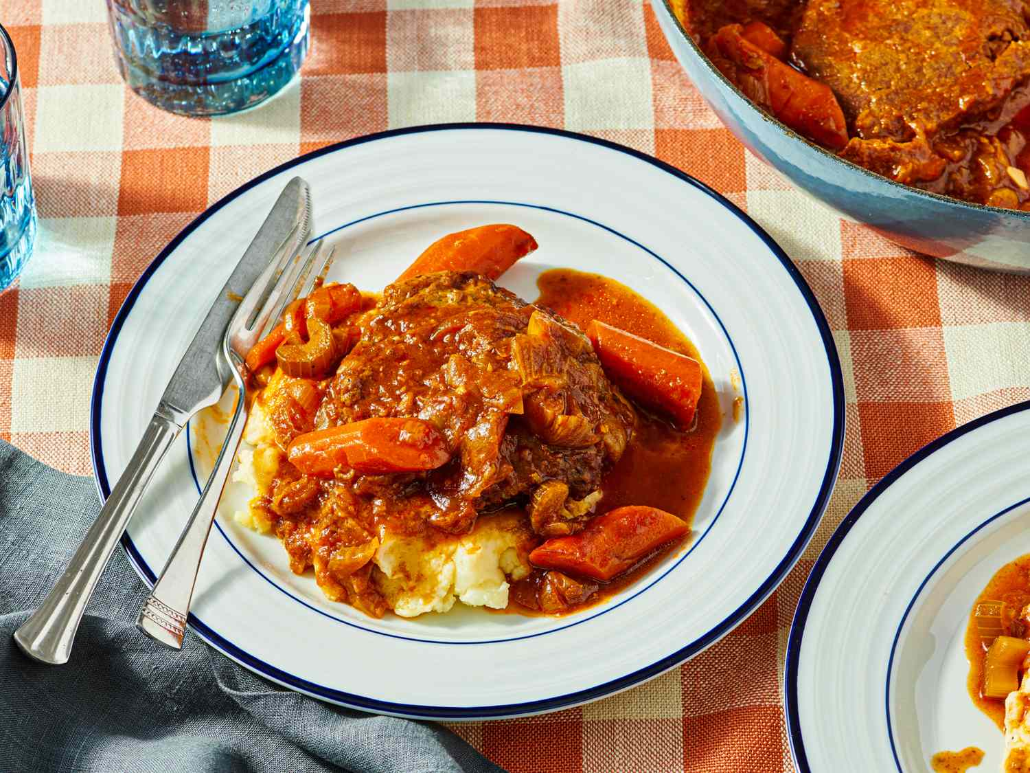 Plate of Swiss steak with carrots and mashed potatoes on a checked tablecloth