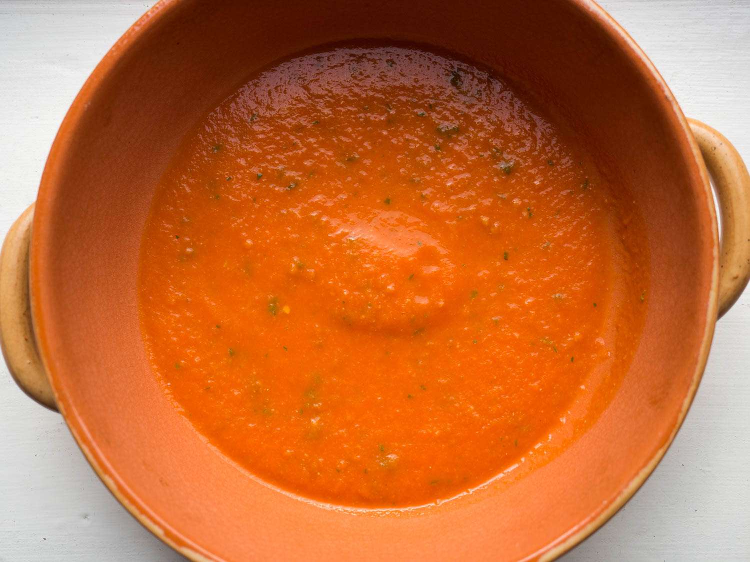 A round earthenware casserole. The bottom of the vessel is covered in a thin layer of tomato sauce.