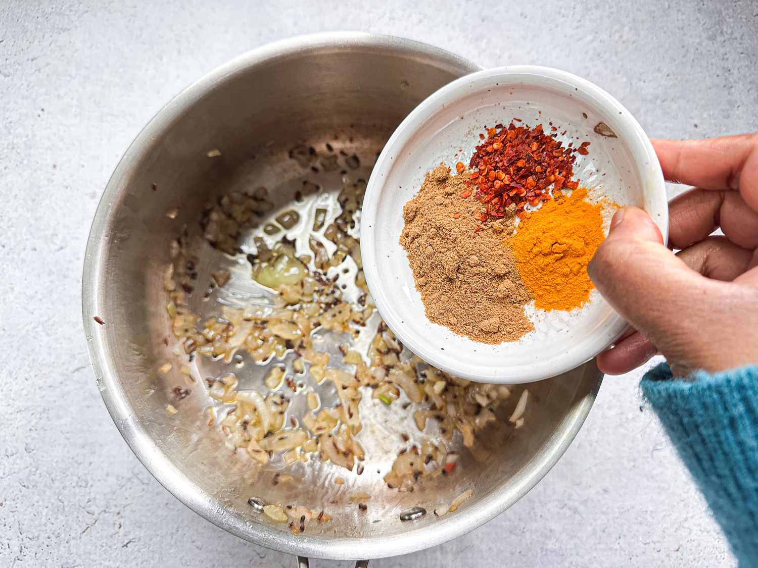 pouring spiced into mixture of cooking onions and garlic 