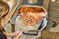 A person removes a pizza from the Ooni Karu 2 Pro Multi-Fuel Pizza Oven