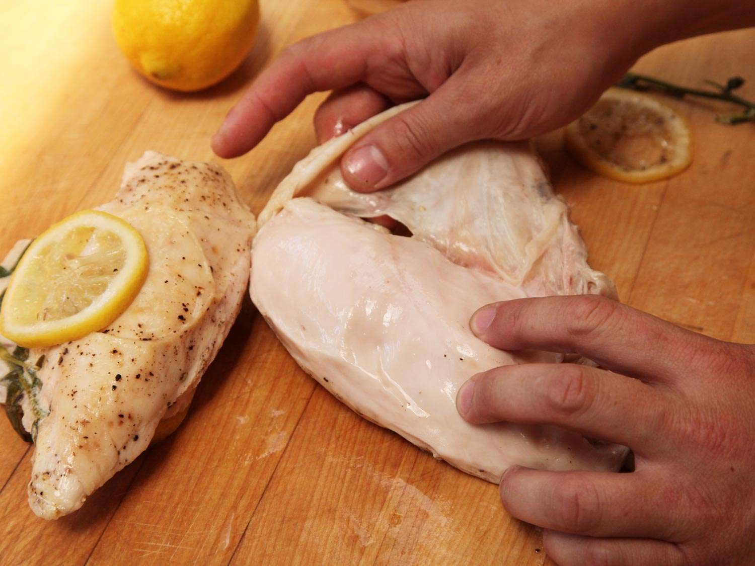 Pulling the skin off the cooked chicken, next to another piece of chicken and a whole lemon.