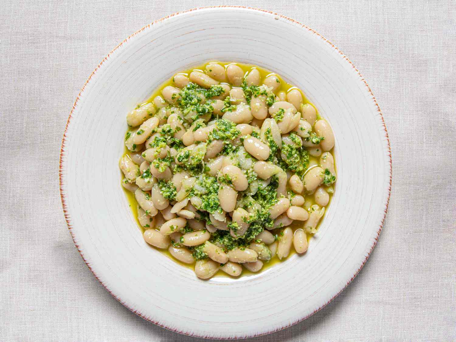 A plate of cooked white beans covered in garlic scape pesto