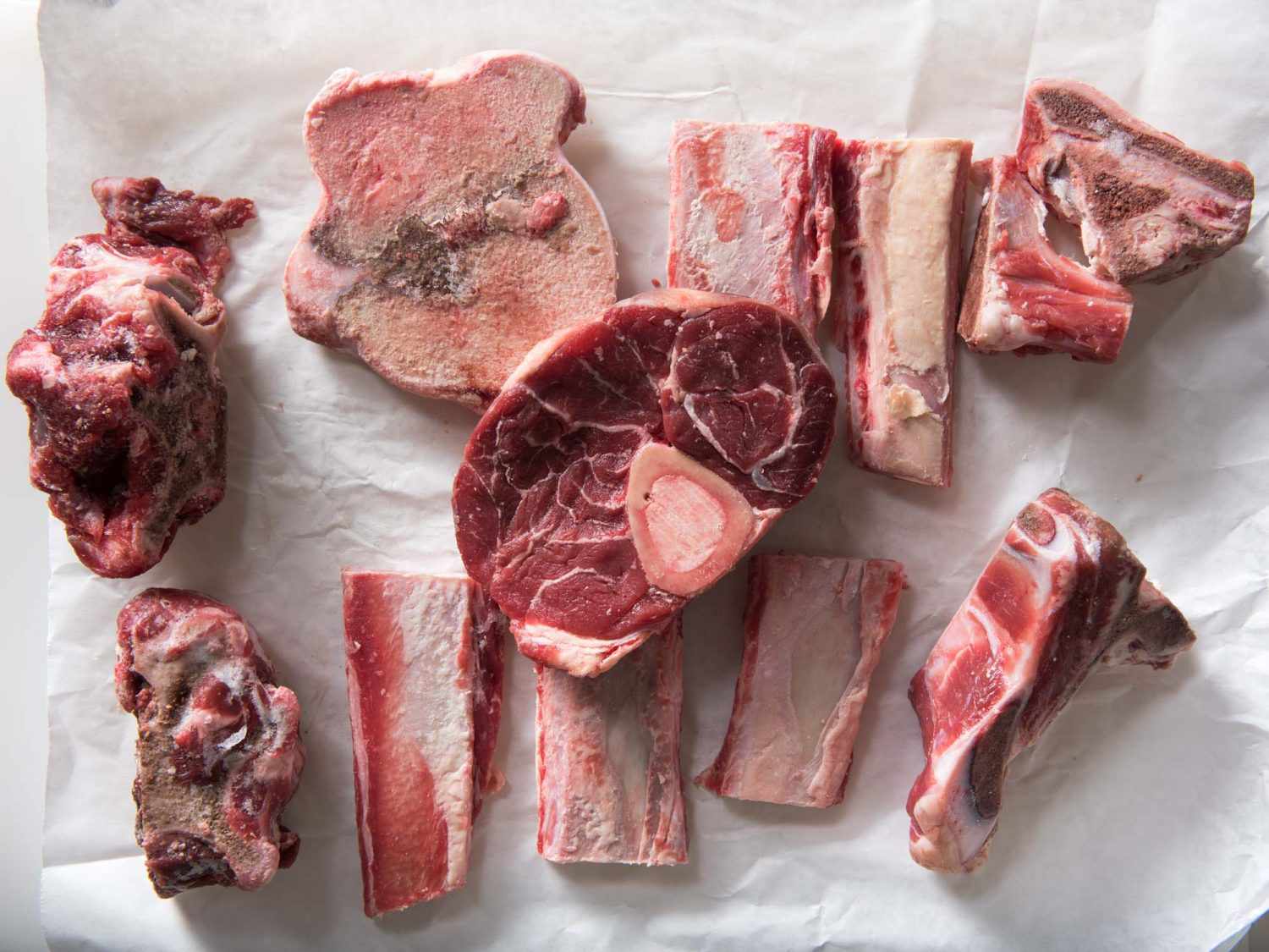 Overhead view of bones and beef cuts for stock laid out on a sheet of parchment.