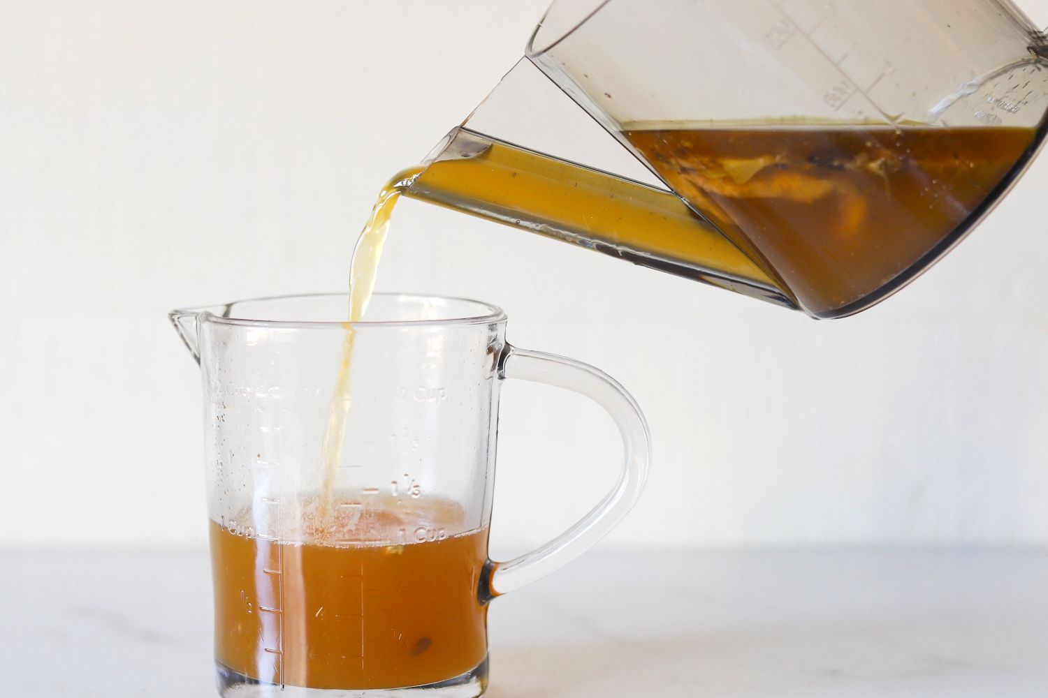 Liquid being poured from a container into a measuring cup on a counter