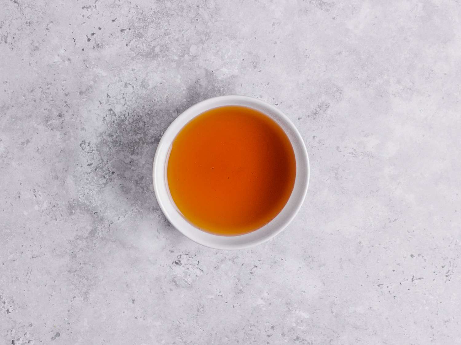 A small bowl of honey on a marbled grey backdrop