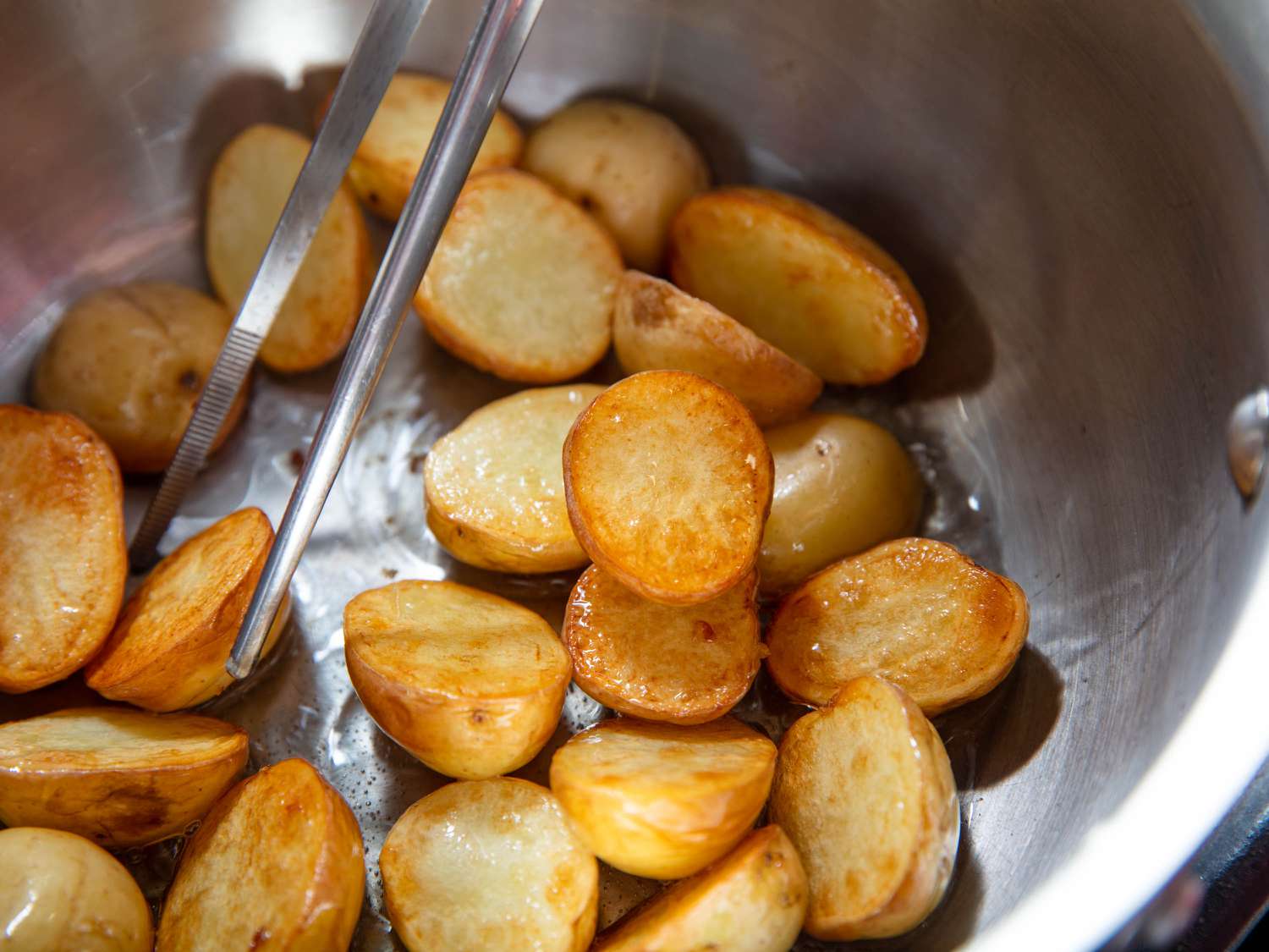 Pan-frying halved Yukon gold potatoes and stirring with metal chopsticks.