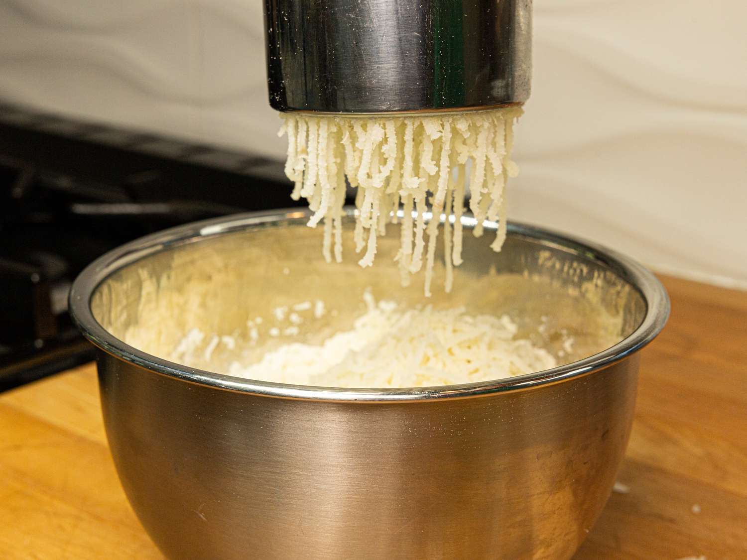 Side view of pushing potatoes through a rice mill into a bowl