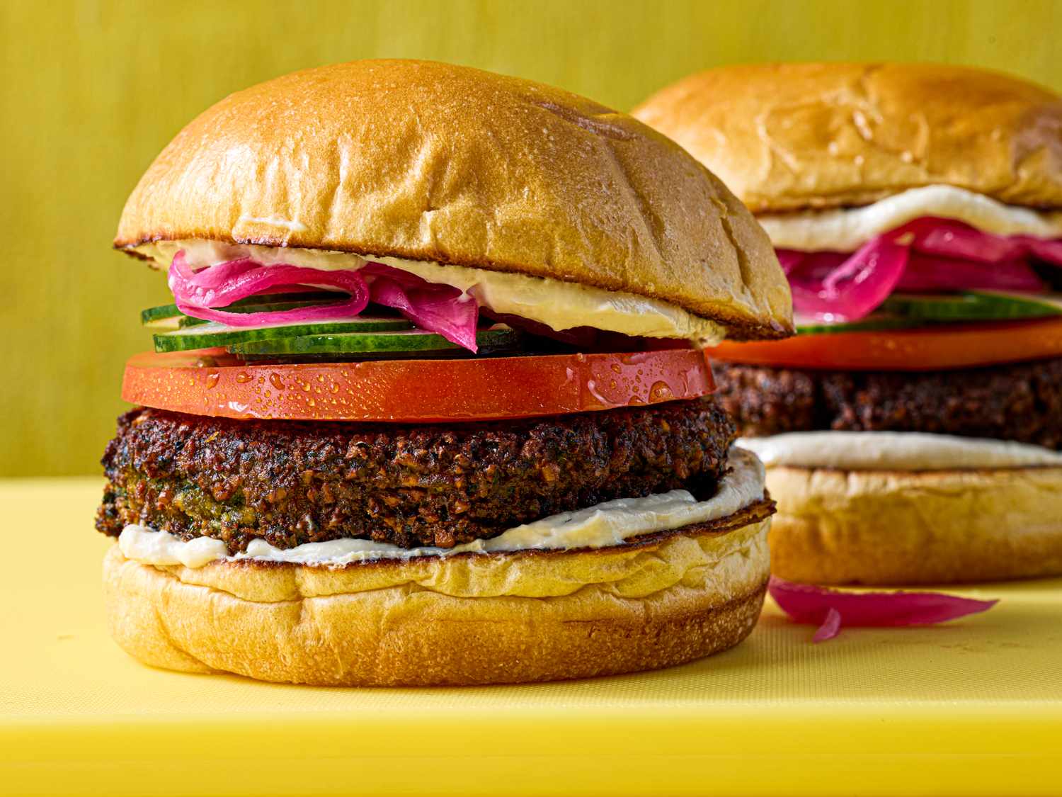 Falafel burgers with tomato cucumber pickled onions and spread on buns displayed on a table