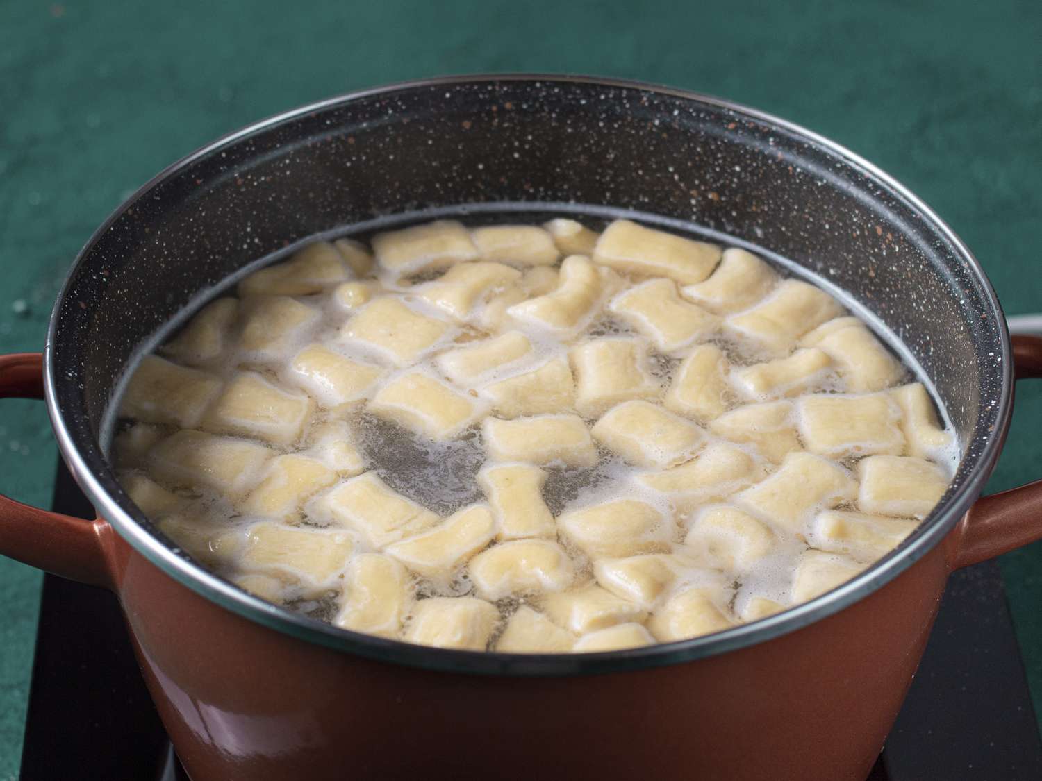 Ricotta gnocchi in a pot of salted water. The gnocchi floating to the top of the water signifies they have finished cooking.
